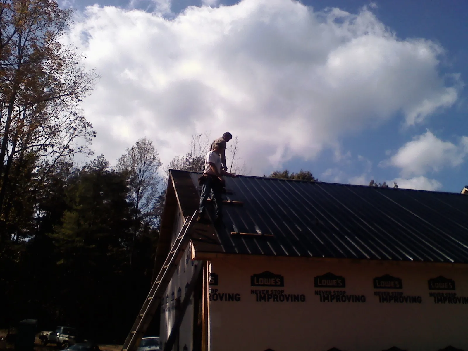 Roofer fastening dark metal panels high against a cloudy sky, from a Roof Inspection job in Crystal River