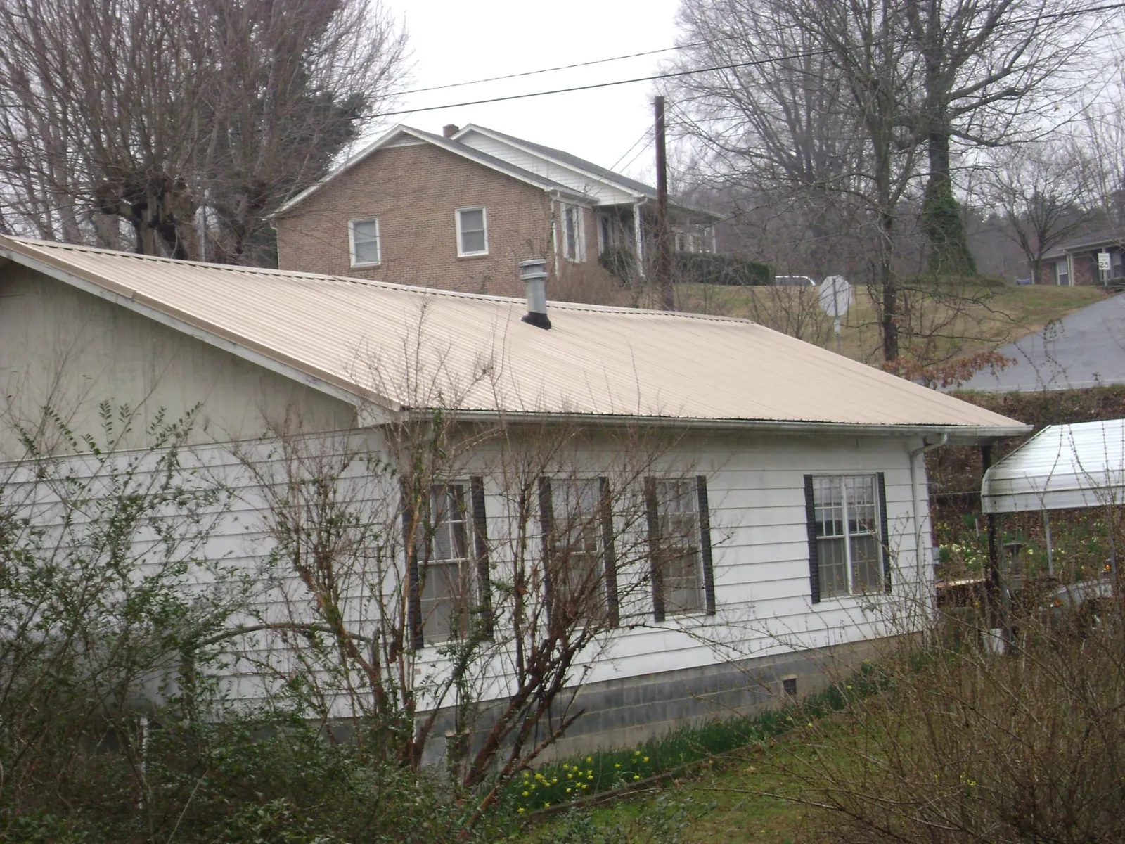 Tan metal roof on a white sided house set into a hillside — Commercial Roofing by Roofing Brothers in Crystal River